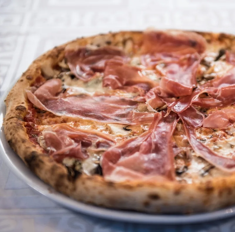 Pizza cu felii subțiri de prosciutto crudo peste mozzarella